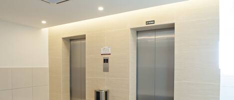 Et moderne elevatormiljø med to elevatorer, en skraldespand og et skilt med elevatorens navn.