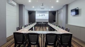 Un salón de conferencias con una larga mesa, sillas y una pantalla proyectora mostrando 'HOTEL ARISSA'.