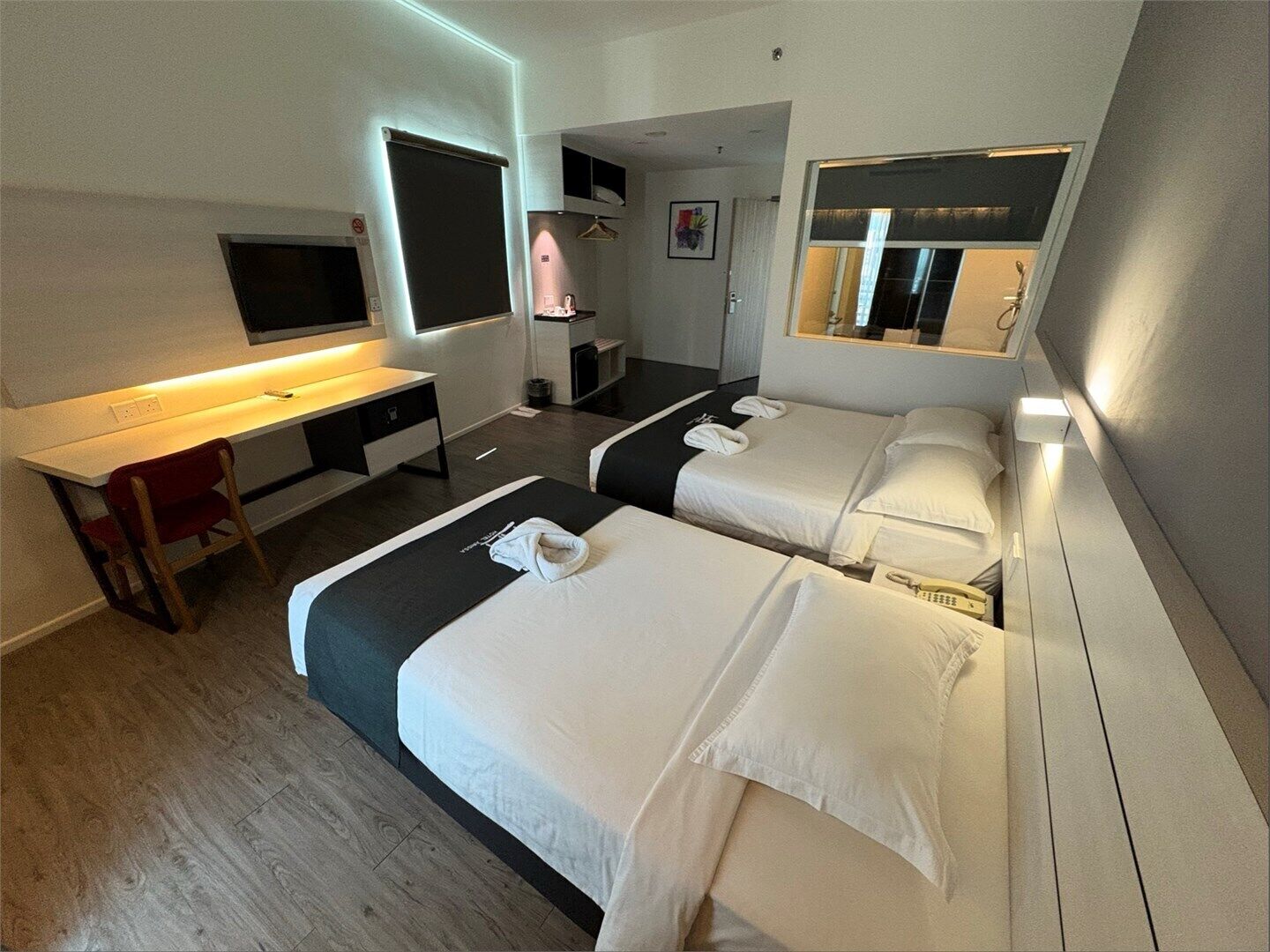 A hotel room with two beds, a desk, a TV, and a mirror.