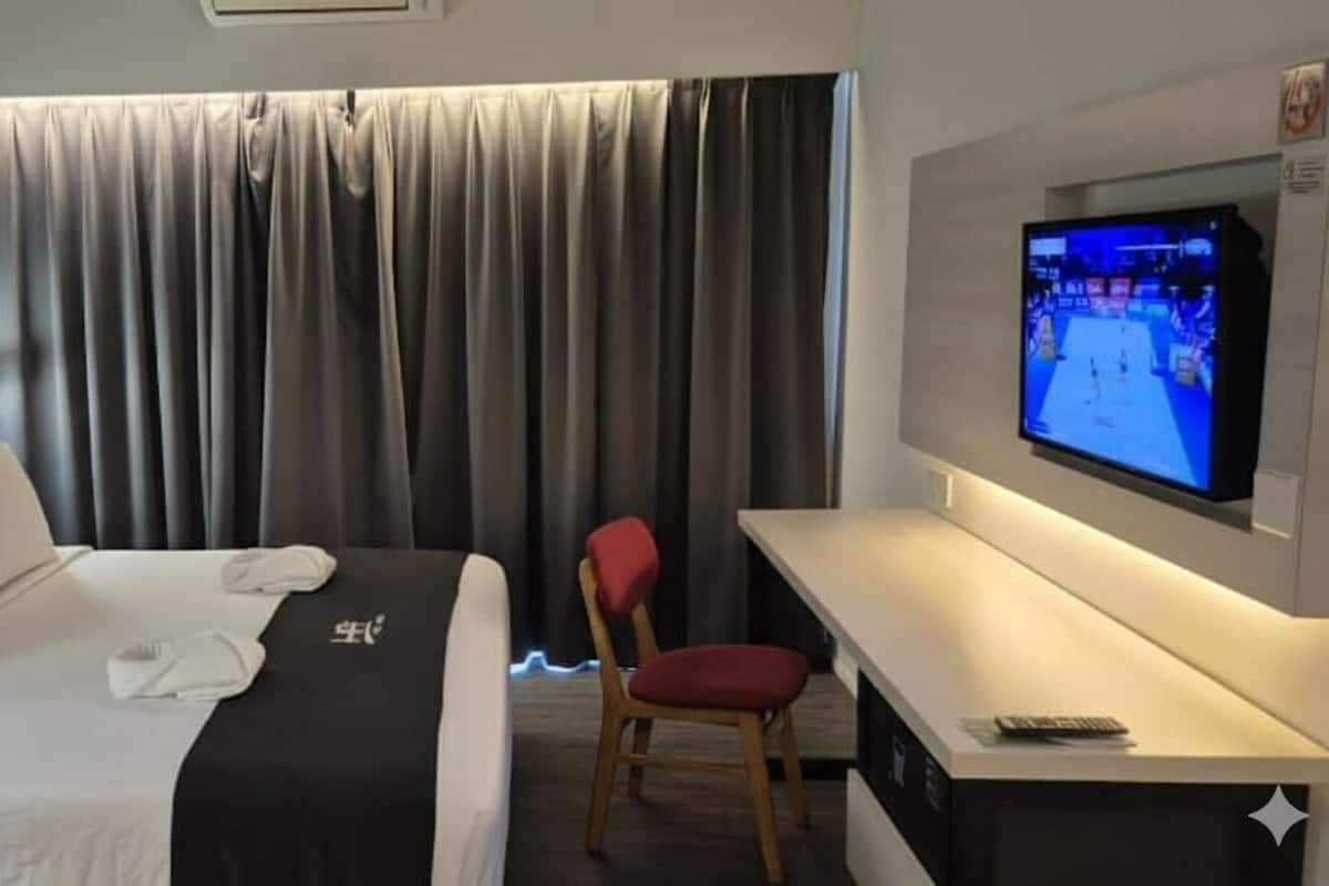 A hotel room with a bed, a desk, a chair, a TV, and a curtain.