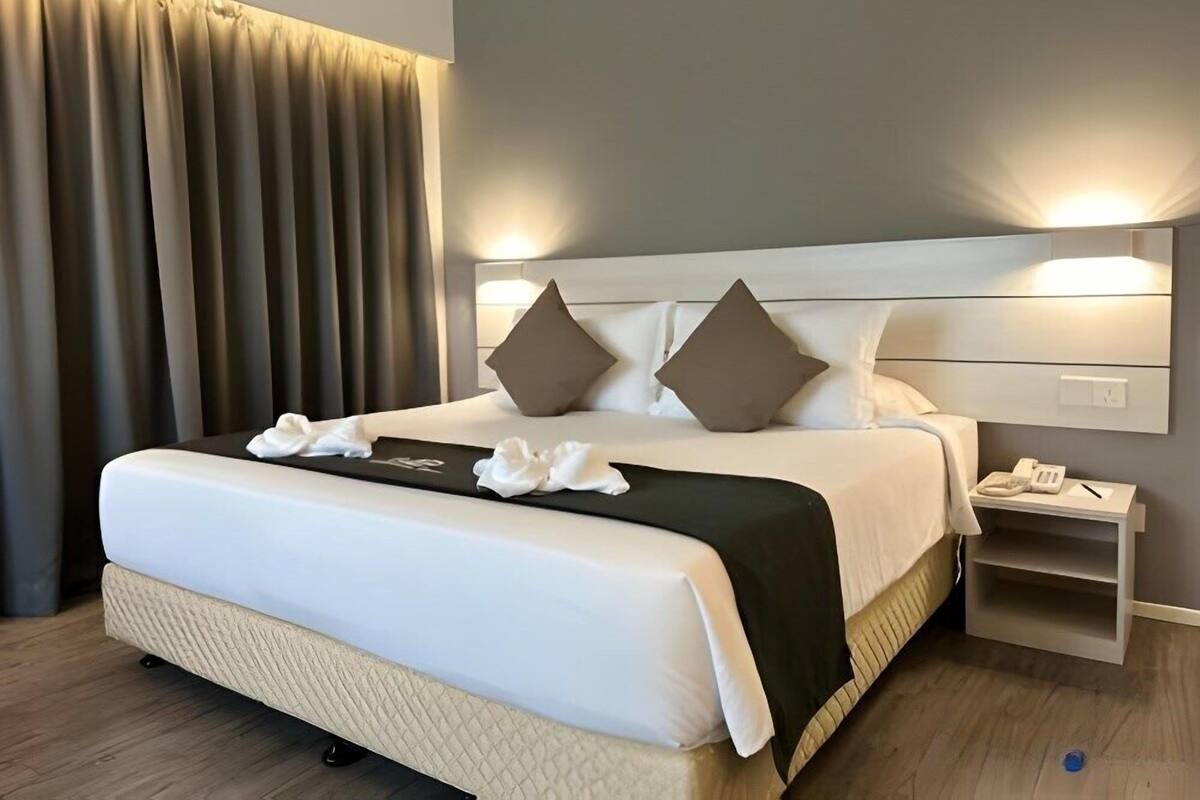 A modern hotel room with a large bed, two pillows, a bedside table with a phone, and a nightstand.