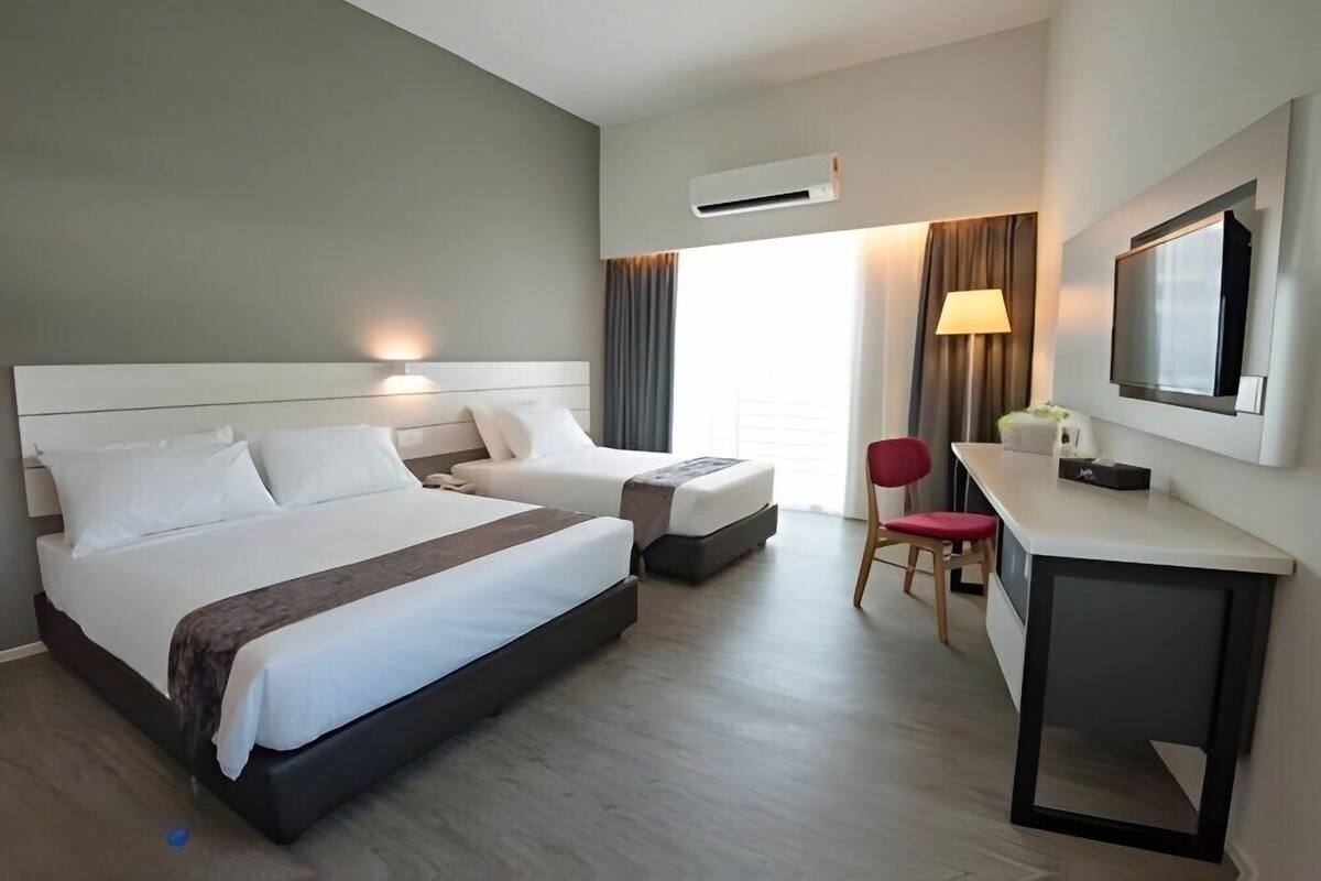 A hotel room with a large bed, a desk, a chair, a TV, and an air conditioning unit.