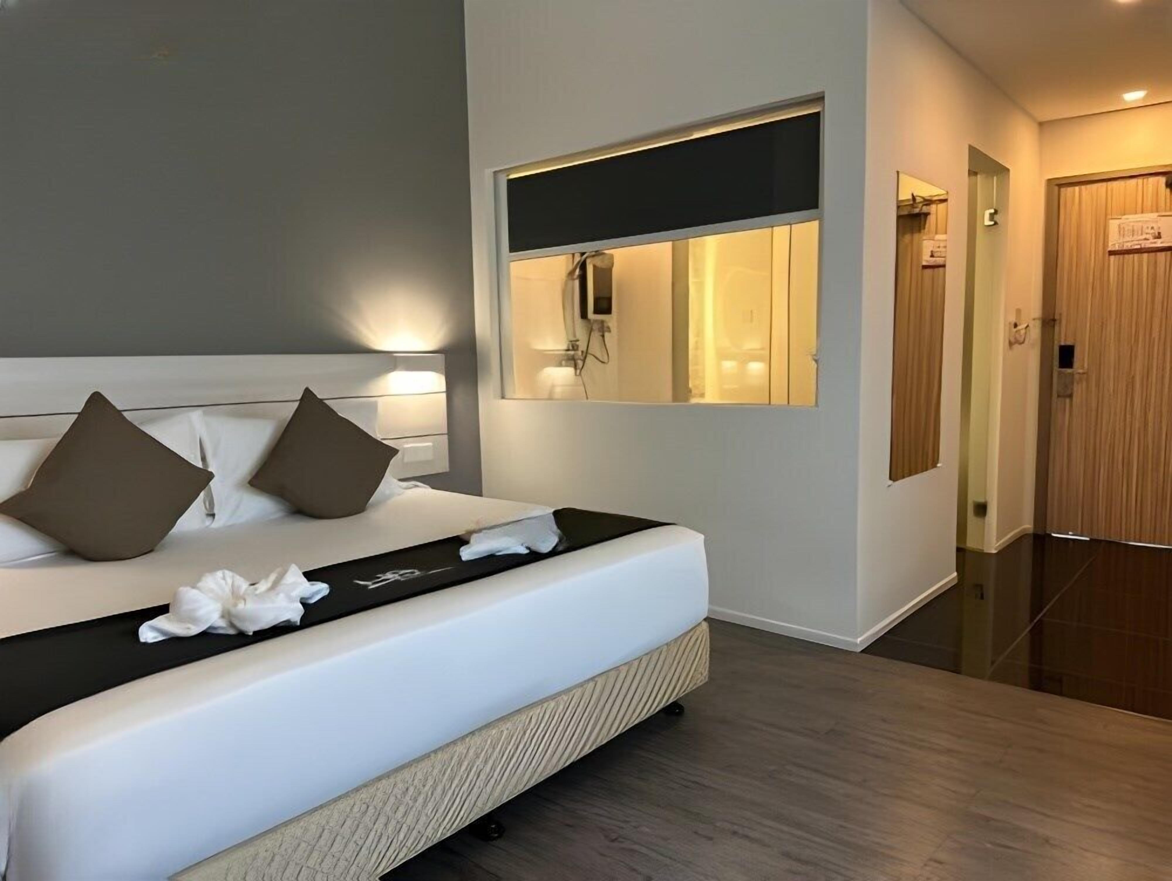 A modern hotel room with a large bed, a bedside mirror, and a wooden door.