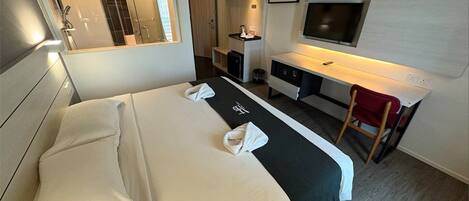 A hotel room with a bed, a desk, a chair, a TV, and a shower area.