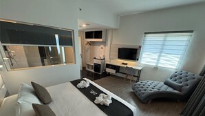 Ett modernt hotellrum med en stor säng, ett skrivbord, en bekväm fåtölj och en TV.