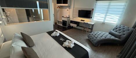 A modern hotel room with a large bed, a desk, a comfortable armchair, and a TV.