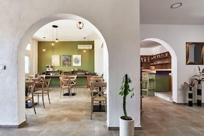 A spacious dining area with high ceilings and arched doorways, featuring a green wall with artwork and a central island with bar stools. - Solano Hotel (Hersonissos)