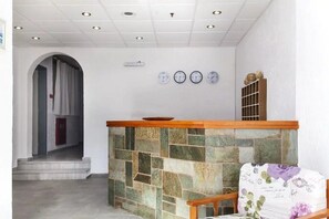 A reception area with a stone wall, a wooden reception desk, and a chair with floral upholstery. - Solano Hotel (Hersonissos)