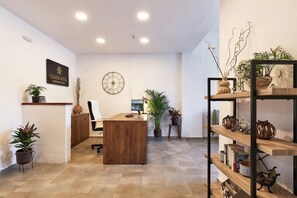 A hotel reception area with a wooden desk, a clock, and potted plants. - Solano Hotel (Hersonissos)