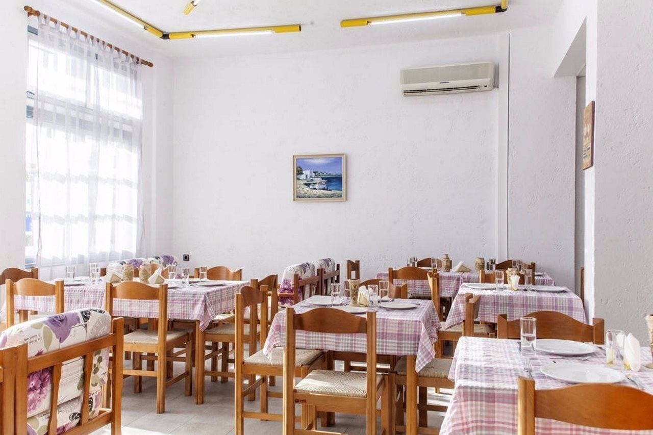 A dining area with multiple tables and chairs, an air conditioning unit on the wall, and a framed picture on the wall.