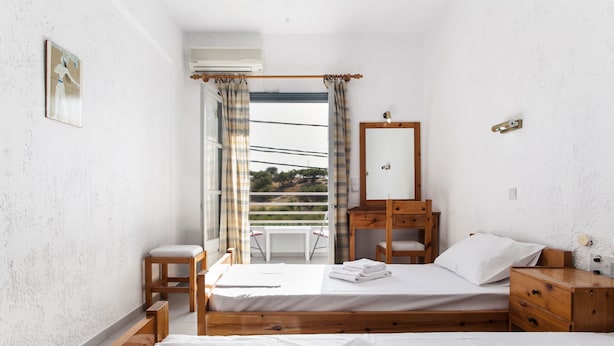 A bedroom with a bed, a wooden dresser, a mirror, and a window with curtains. - Solano Hotel (Hersonissos)
