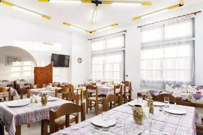 A dining area with multiple tables set for meals, wooden chairs, and a television mounted on the wall. - Solano Hotel (Hersonissos)