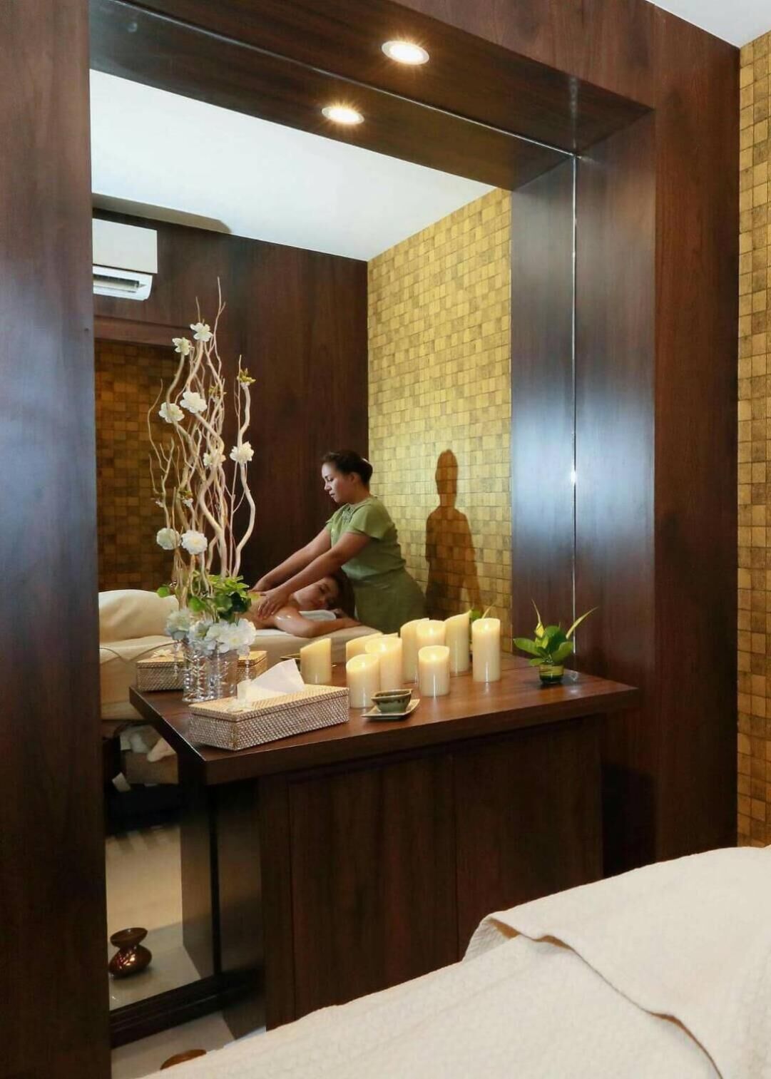 A spa room with a wooden reception desk, a mirror, and a statue of a person meditating.
