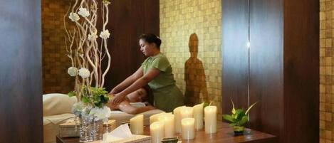 A spa room with a wooden reception desk, a mirror, and a statue of a person meditating.