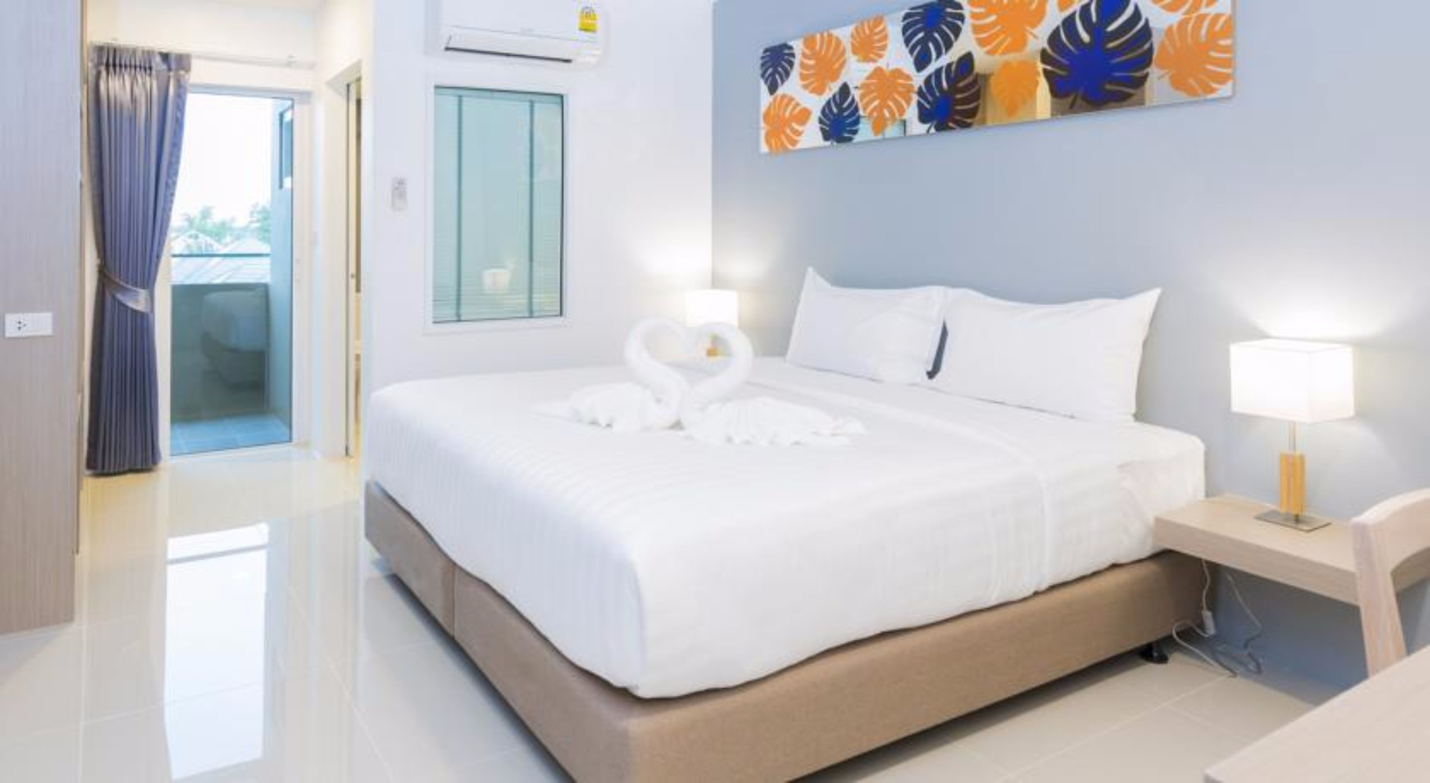 A hotel room with a large bed, a nightstand with a lamp, a wall with a leaf pattern, and a door with curtains.