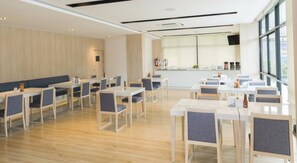 A modern dining area with wooden flooring, white tables, and grey chairs. There are large windows providing natural light and a view of the outside. - Trat City Hotel (Trat)