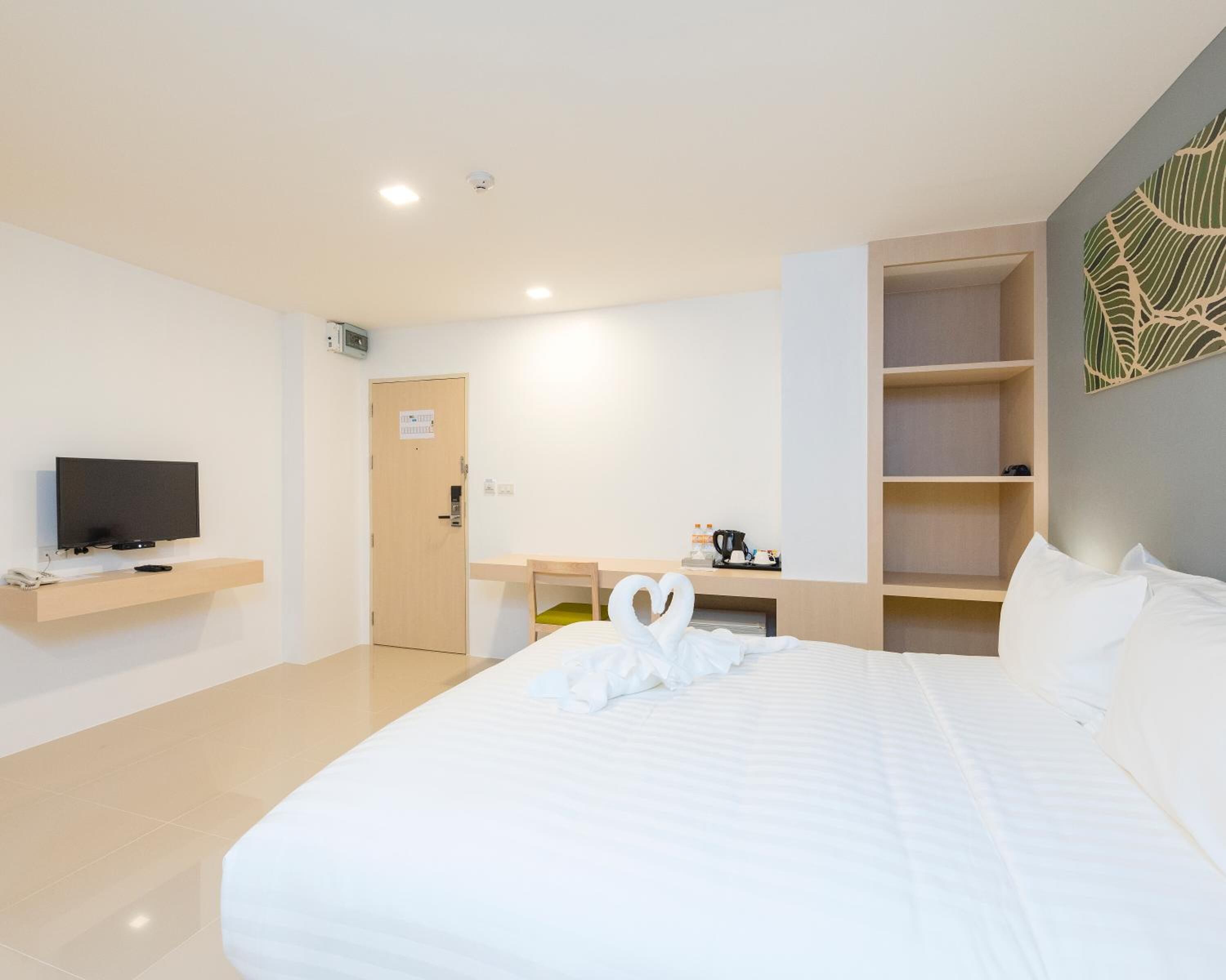 A hotel room with a bed, a television on a shelf, a desk with a chair, and a coffee maker.