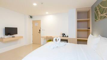 A hotel room with a bed, a television on a shelf, a desk with a chair, and a coffee maker.