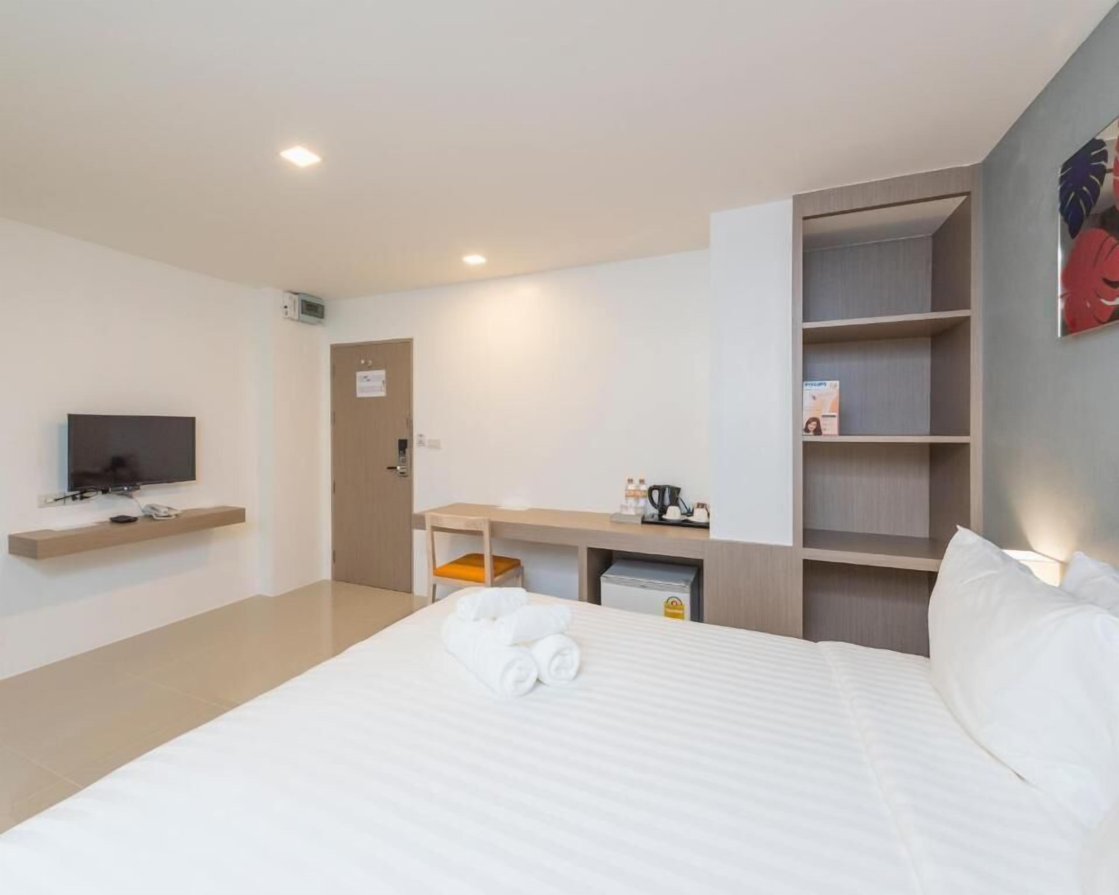 Una habitación de hotel moderna con una cama grande, un escritorio con silla, un televisor y estanterías integradas.