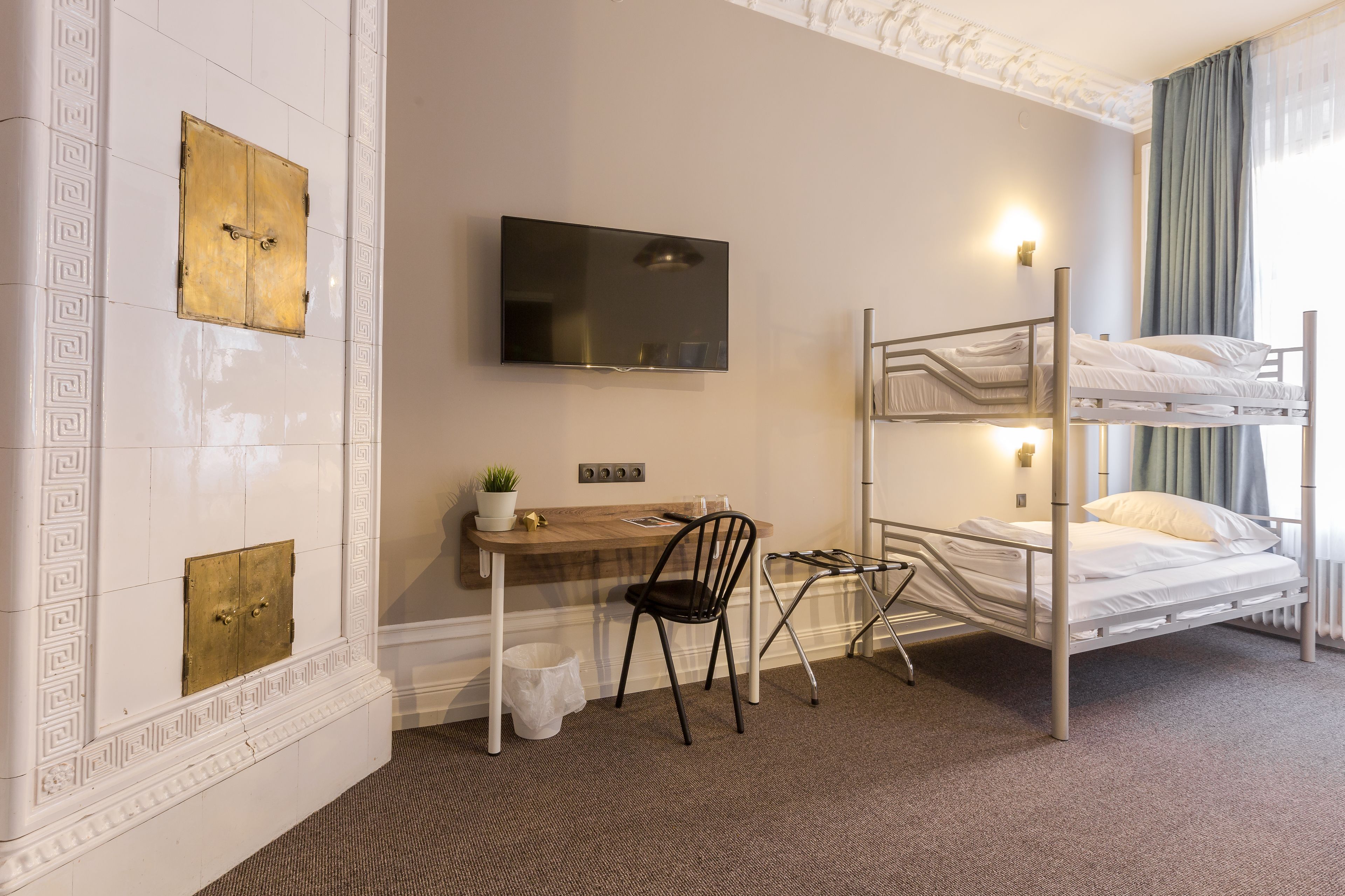 A room with a bunk bed, a desk with a chair, a TV, and a small plant.