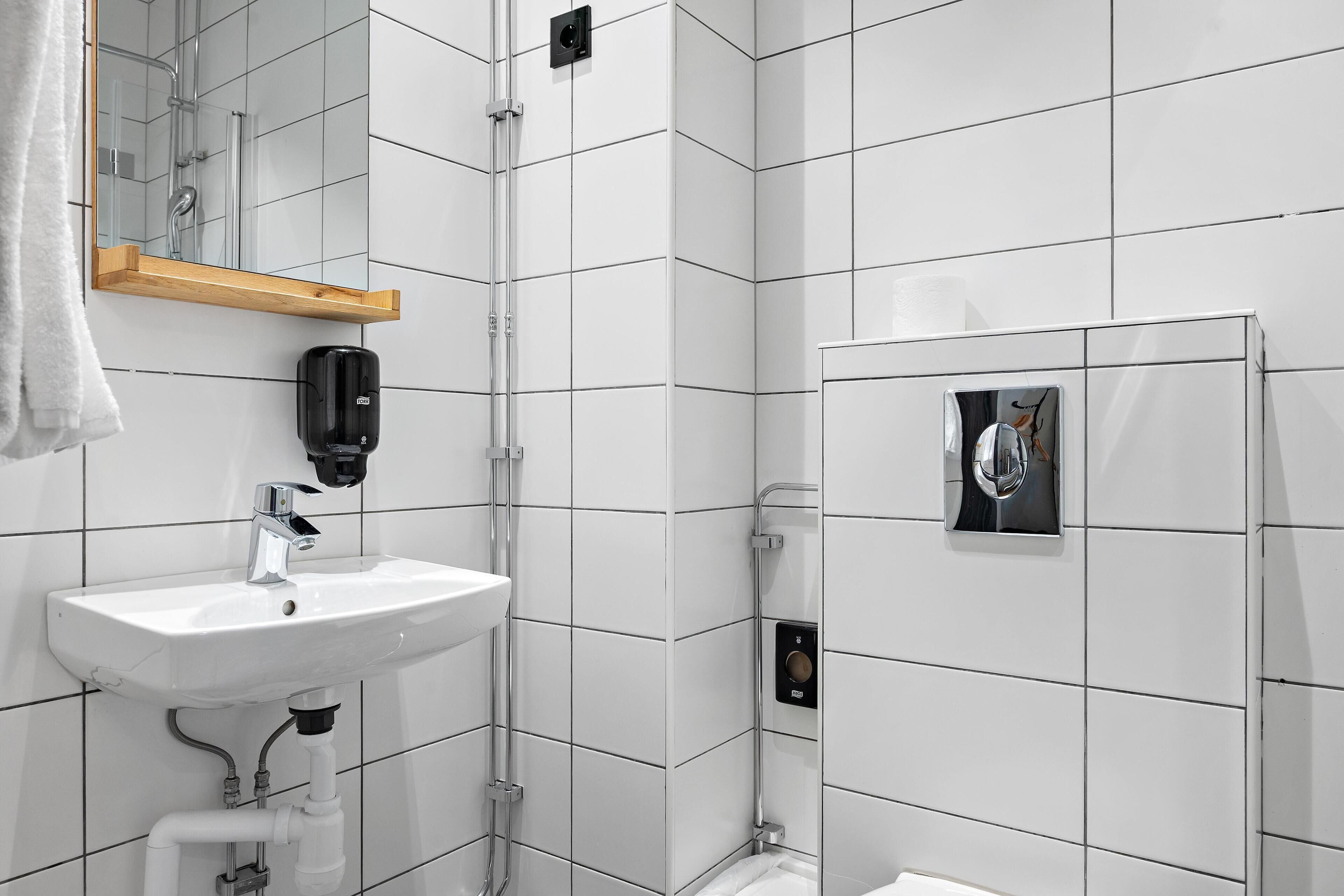 A modern bathroom with a white sink, mirror, and tiled walls.