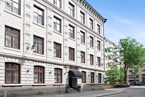 En byggnad med flera våningar i en klassisk arkitektonisk stil, med stora fönster och en framträdande entré som har ett svart markis.