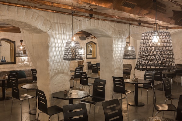 An interior with stone arches, black chairs, round tables, and hanging lamps. - Hotel Hotorget, BW Signature Collection (Stockholm)
