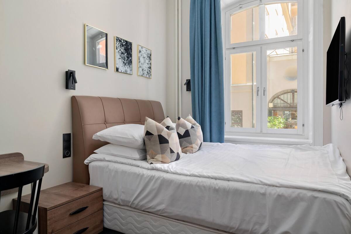 Ett välstädat hotellrum med en säng, ett sängbord och ett fönster med gardiner.