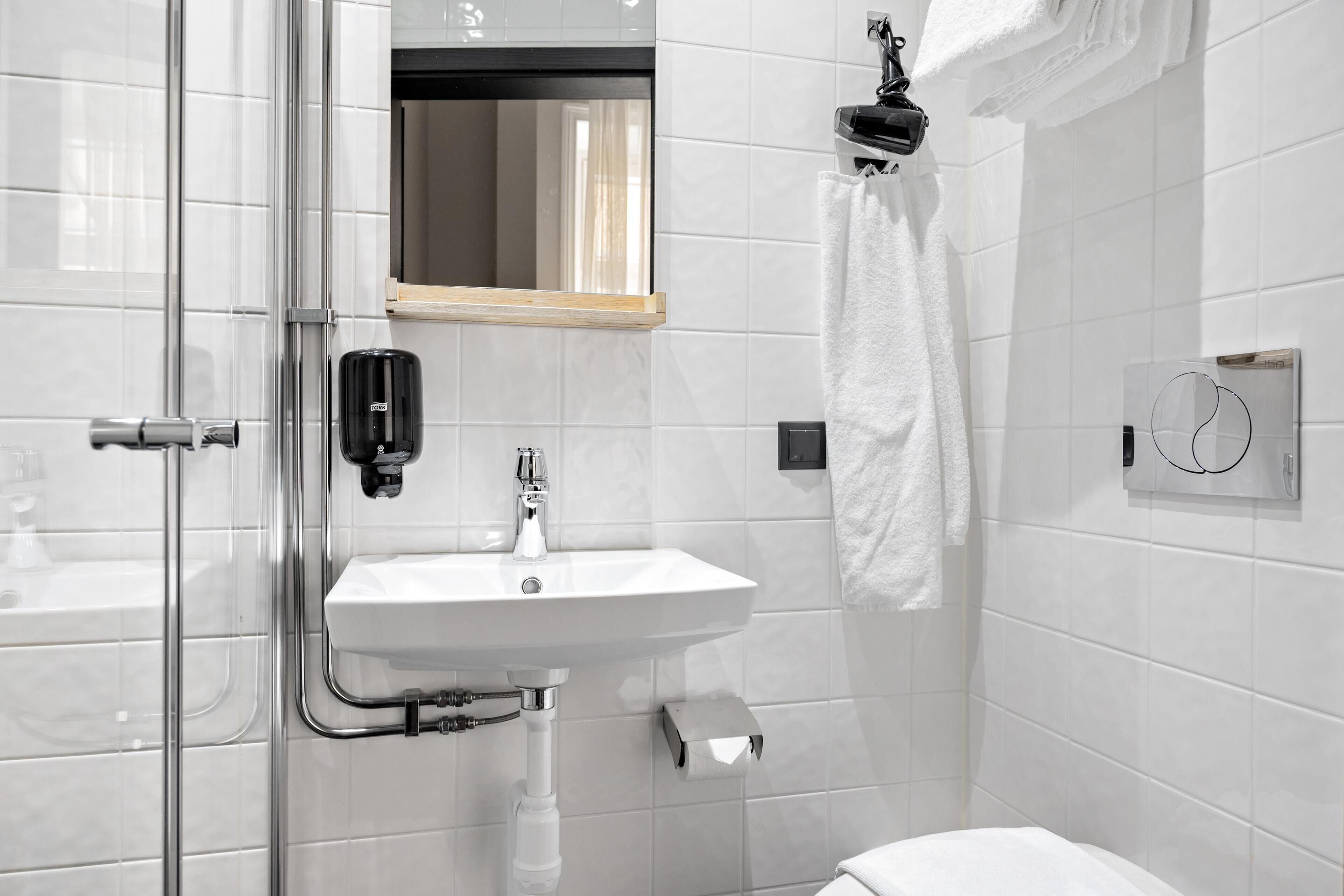 A bathroom with a glass shower enclosure, a white sink, a mirror, and a towel rack.