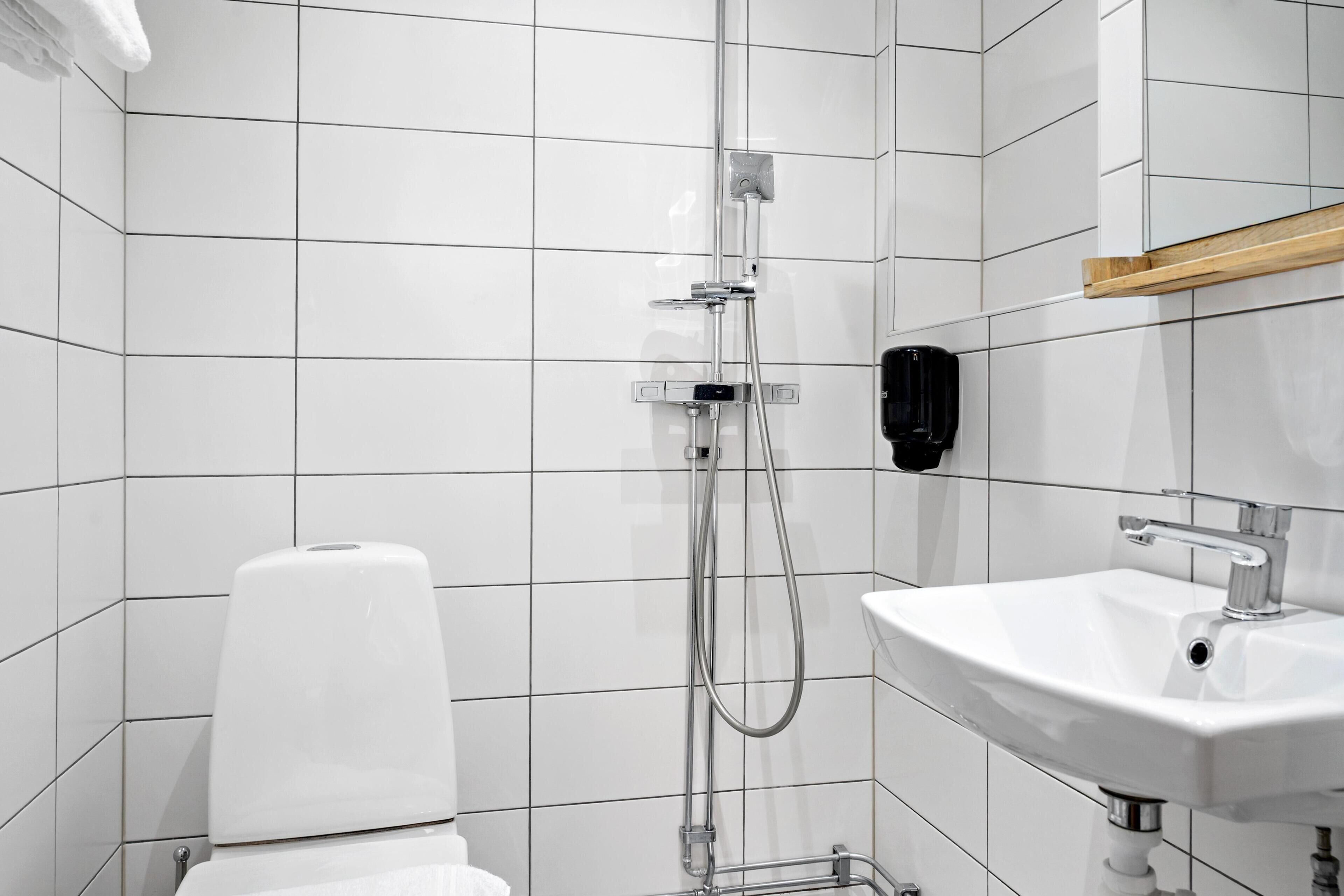 Un bagno moderno con piastrelle bianche, una doccia, un water e un lavandino.