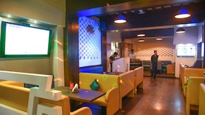 A restaurant with booths and tables, a TV screen, and a counter area. - Evergreen Hotel (Mumbai)
