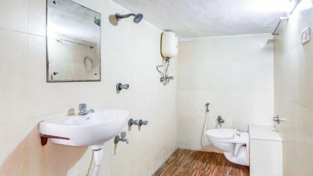 A bathroom with a sink, mirror, toilet, and shower. - Evergreen Hotel (Mumbai)