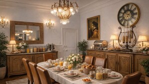 Comedor con una larga mesa dispuesta para el desayuno, armarios de madera, un candelabro y un reloj grande en la pared.