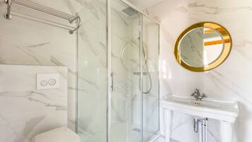 Un bany modern amb una cabina de dutxa de vidre, un vàter blanc i un lavabo amb un mirall de marc daurat.