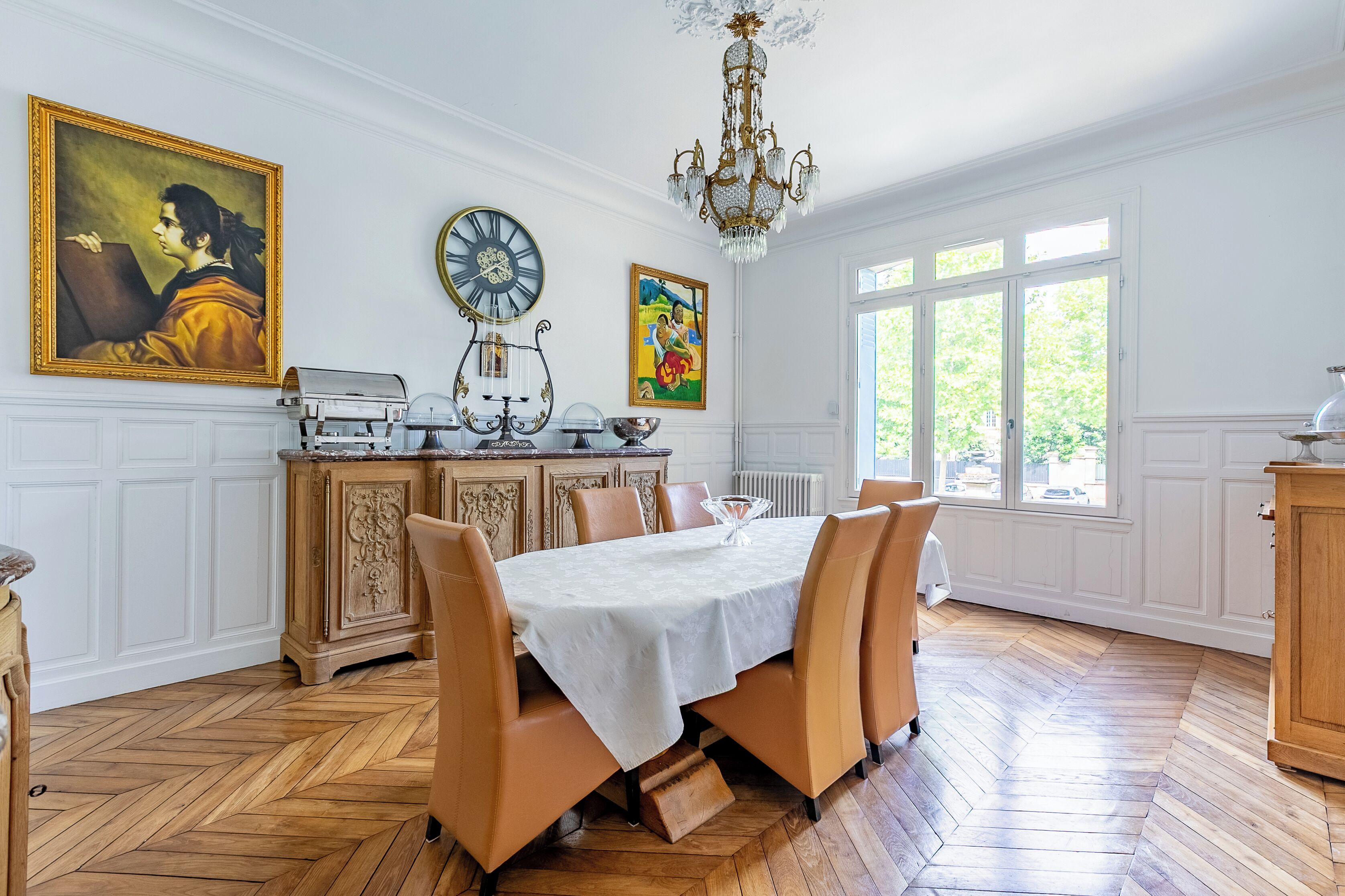 Ein Esszimmer mit großem Tisch, Stühlen, einer Kandelaber und Kunstwerken an den Wänden.