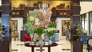 A lobby with a round table displaying floral arrangements, a red chair, and a modern interior with abstract art.