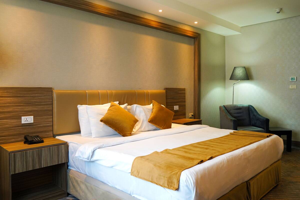 Une chambre d’hôtel avec un grand lit, une table de chevet avec une lampe, une chaise et un bureau avec un téléphone.