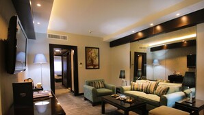 A modern hotel room with a sofa, armchairs, a coffee table, and a flat-screen TV.