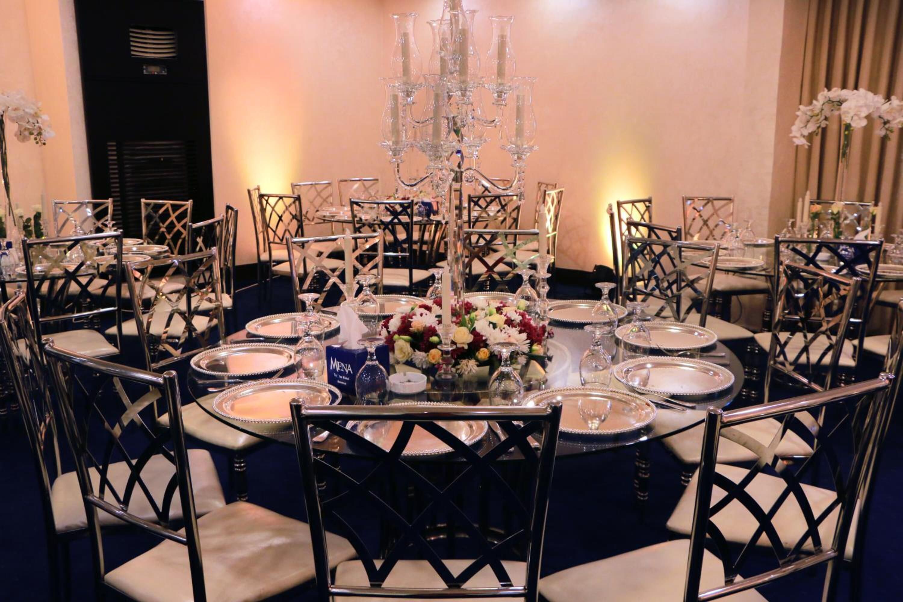 Un comedor formal con mesas redondas, sillas elegantes y una lámpara de araña central.