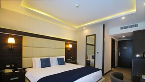 A hotel room with a large bed, bedside lamps, a desk, and a chair.