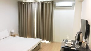 Quarto de hotel com cama, escrivaninha com cafeteira, televisão e cortinas.