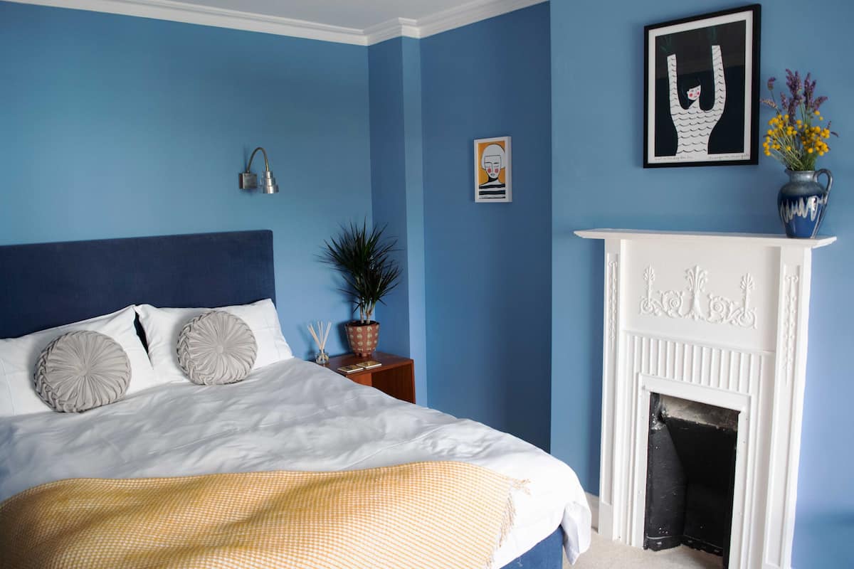 A bedroom with a bed, a white fireplace, and blue walls.