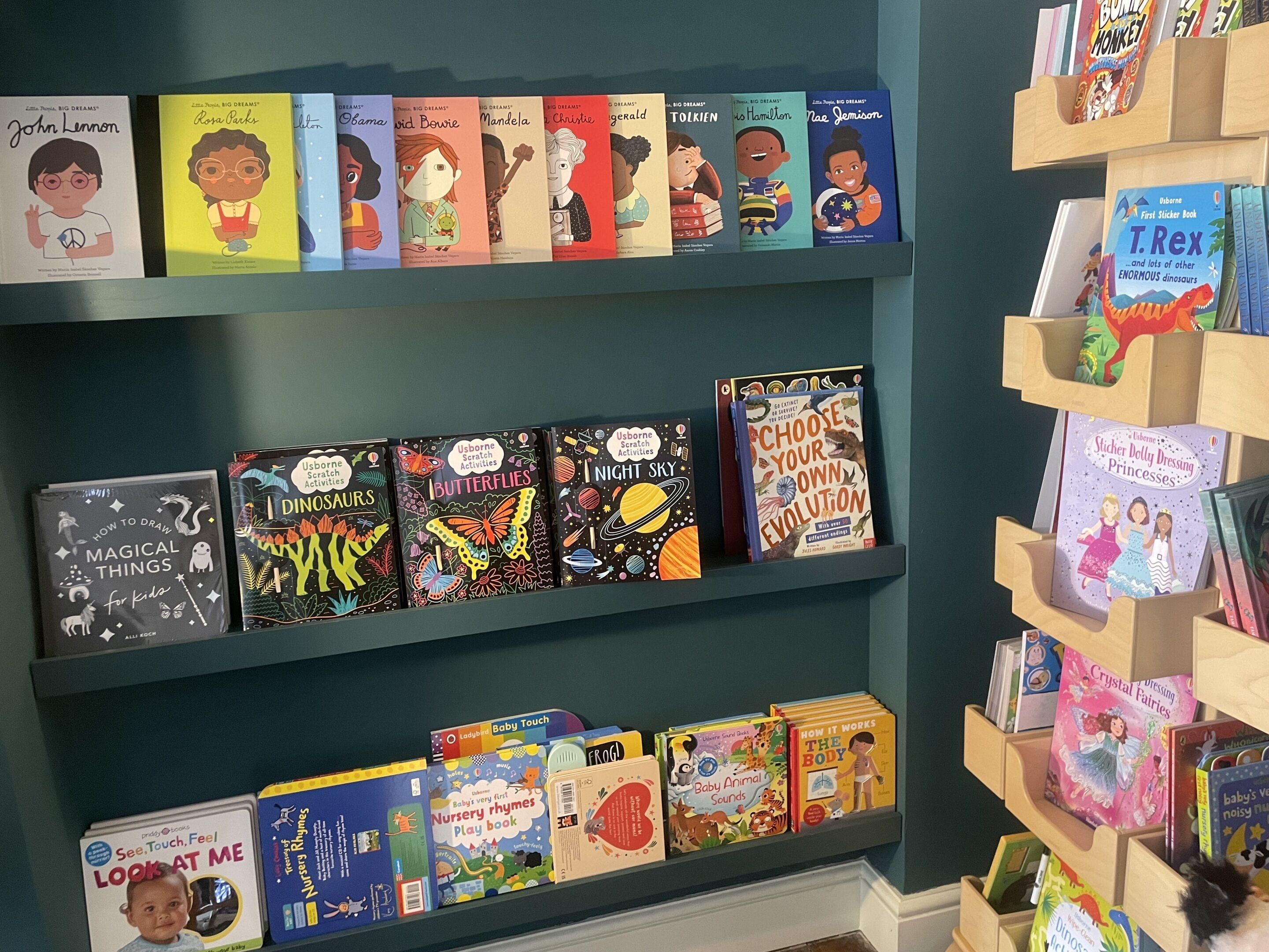 A bookshelf with children's books, including titles like 'John Lennon' and 'Dinosaur.'