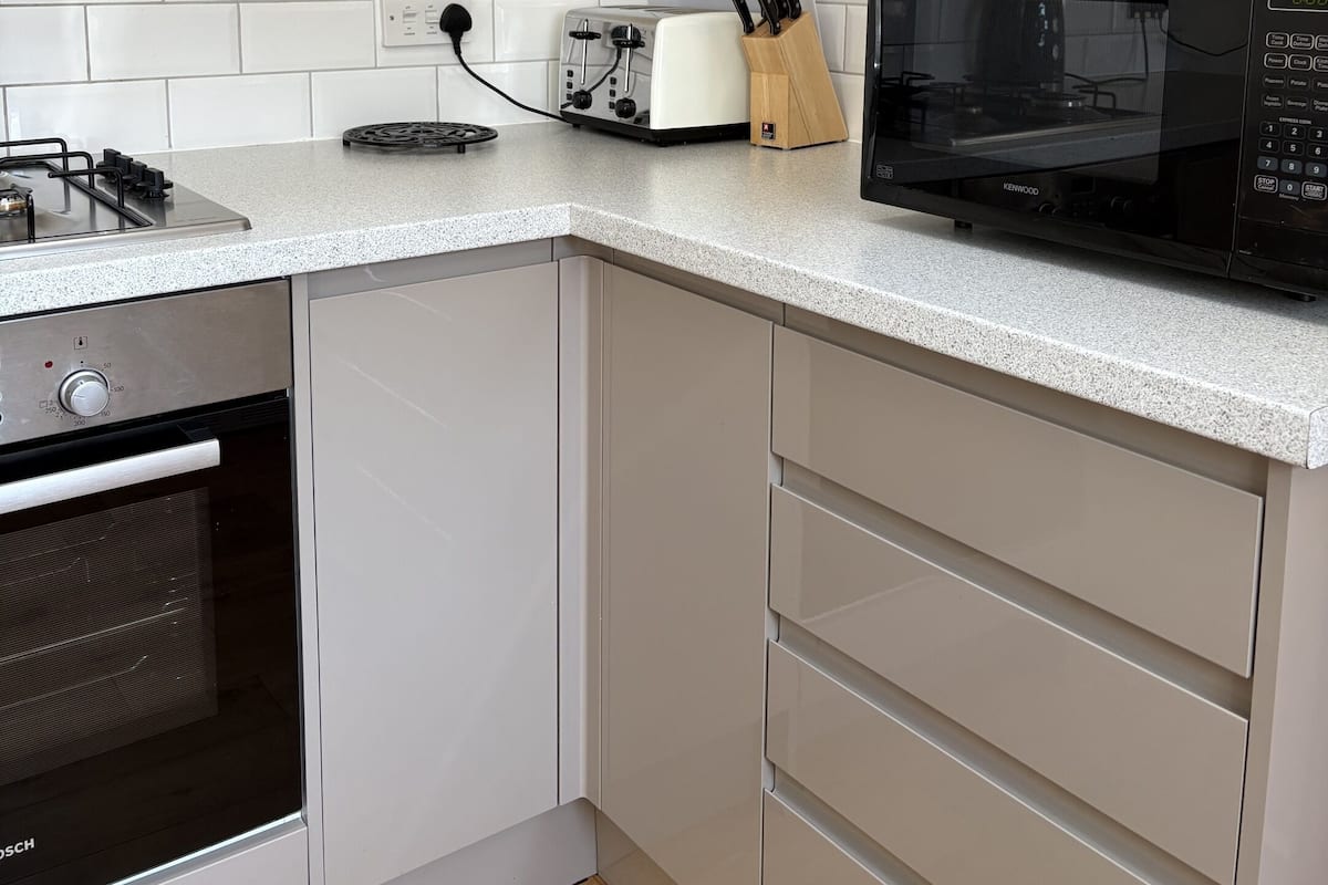 A kitchen with white cabinets, a Bosch oven, a Kenwood microwave, and a toaster.