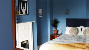 Un dormitorio con un espejo grande, una cama con ropa de cama blanca, una mesita de noche con lámpara y una chimenea.