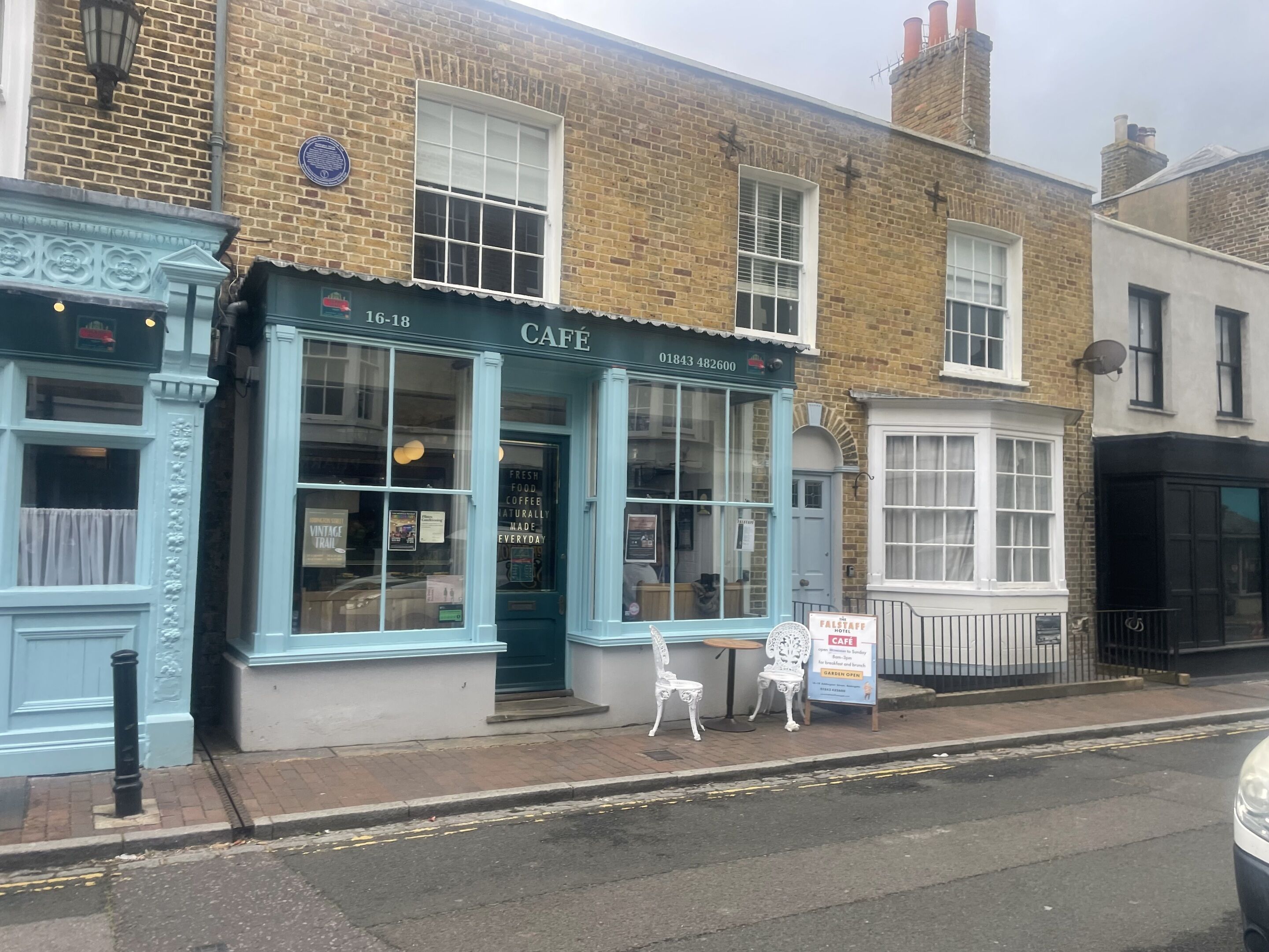 A café with a blue exterior, a visible phone number, and a sign indicating it is open for garden and breakfast.