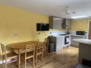 Une cuisine compacte comprenant une table à manger, des chaises, un téléviseur fixé au mur, un four à micro-ondes et une cuisinière.
