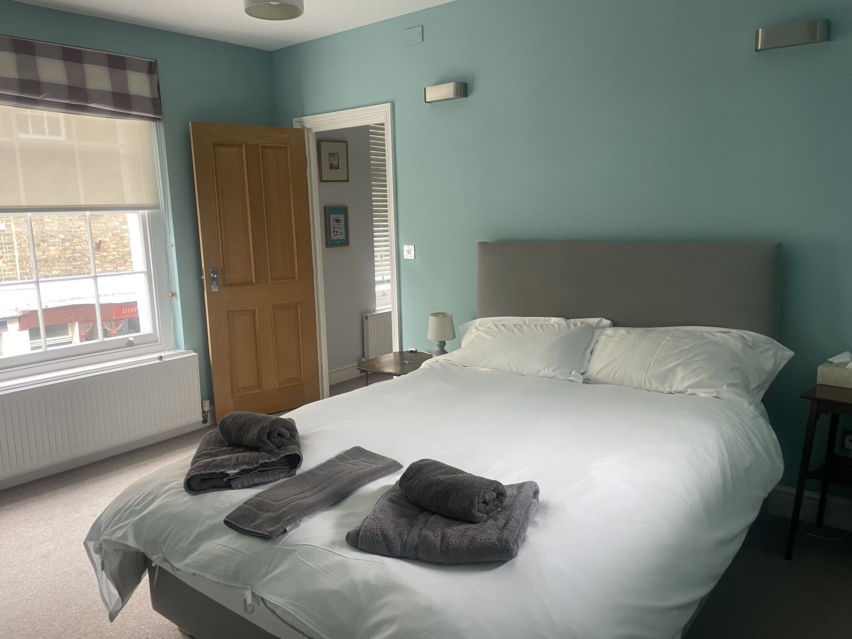 Une chambre à coucher avec un lit, des serviettes, une fenêtre, une porte et un radiateur.