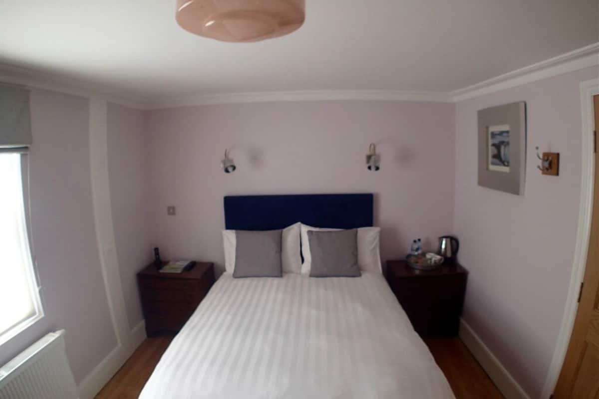 A bedroom with a large bed, two bedside tables, a nightstand, a window, and a wall-mounted light fixture.