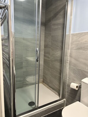 A glass-enclosed shower stall with a toilet and towel rack in a modern bathroom.